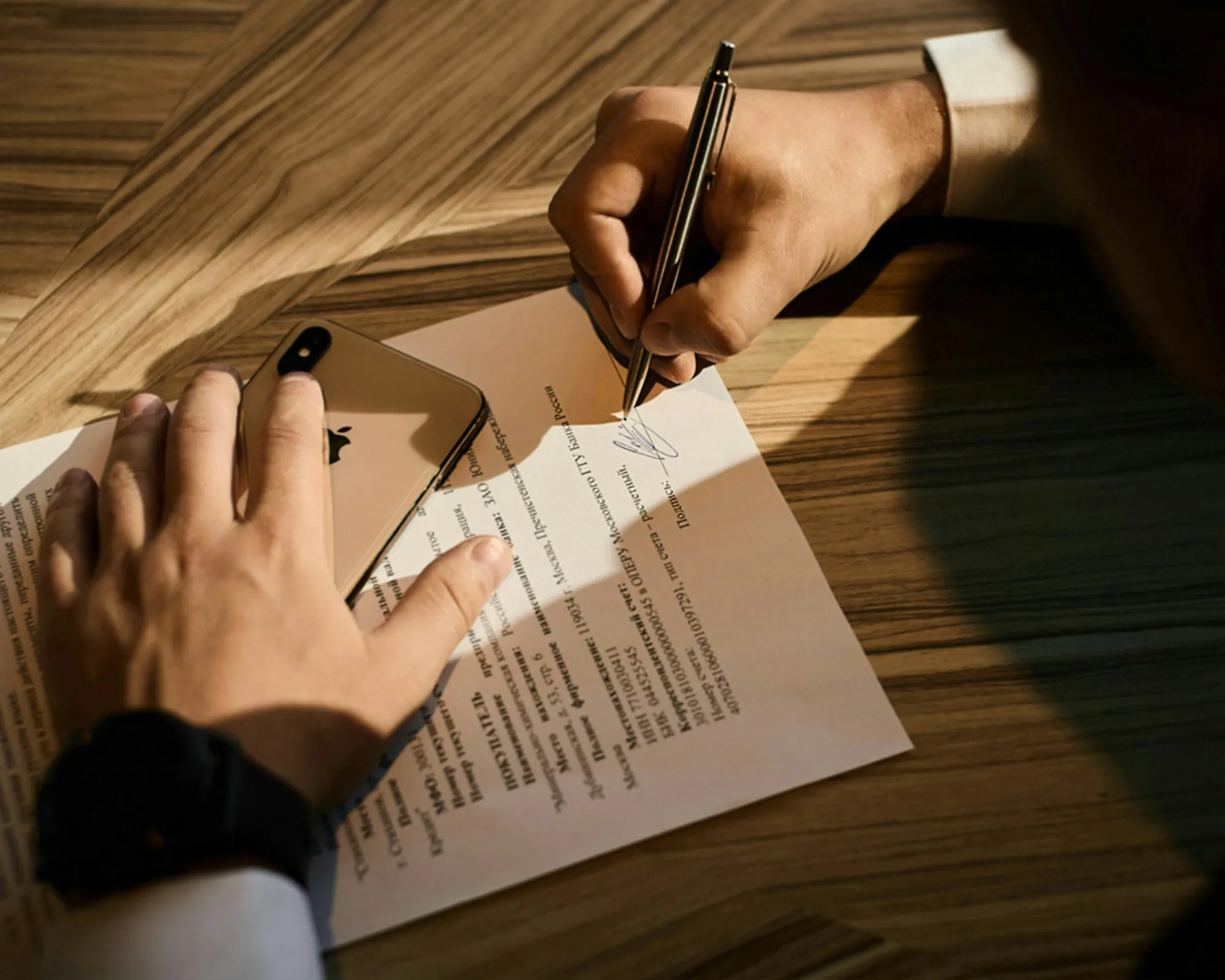 Hand signing a document on a wooden table